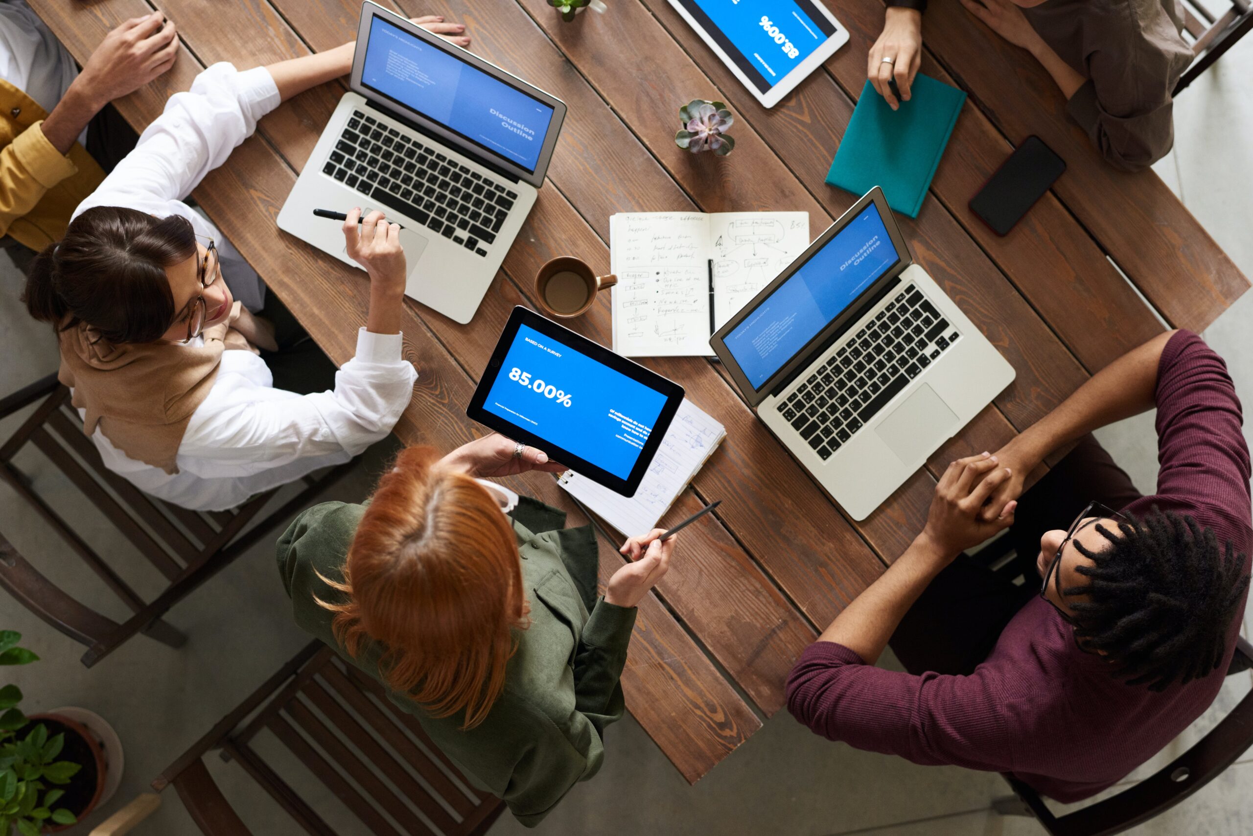 A group of people are sitting at a table, they have laptops in front of them and are collaborating.