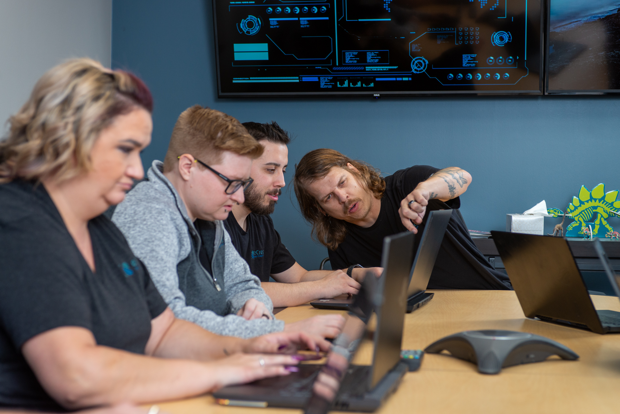 4 IT technicians sit in front of their laptops working together